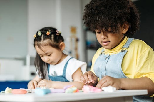 Two kids enjoy creative play with clay at a kindergarten table indoors.
